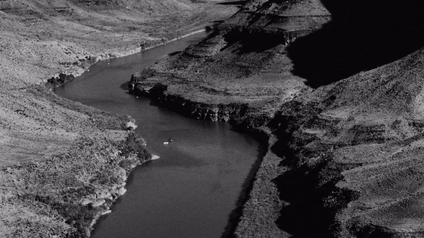 A river bends through a deep canyon, exposing layered rock strata lit by low evening sun.